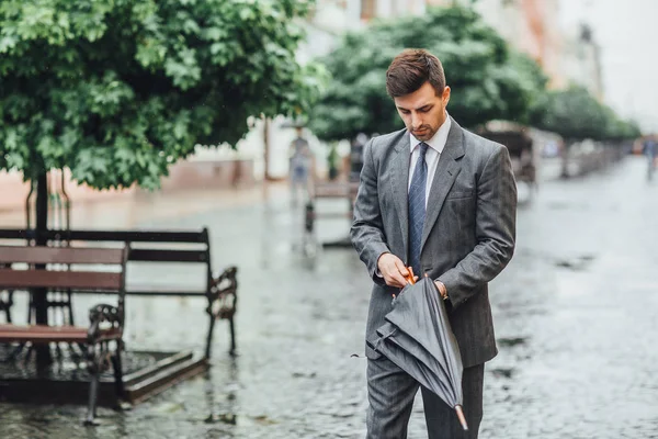 Attractive businessman going down street and looking at grey umbrella