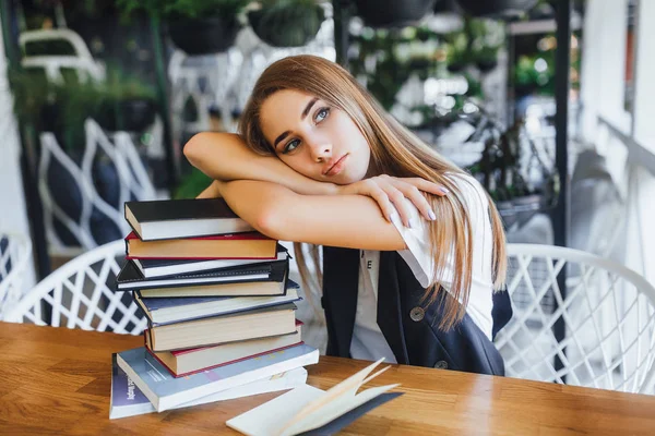 young woman leaned on books at cafe, focus on foreground