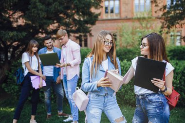 Kampüs yakınında konuşan iki genç kadın, arka planda arkadaşlar
