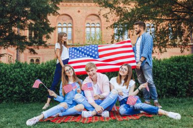 kampüsün arka planında duran Amerikan bayrağına sahip öğrenci grubu