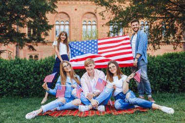 kampüsün arka planında duran Amerikan bayrağına sahip öğrenci grubu