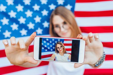 Amerikan bayrağının arka planında selfie çeken genç bir kadın.