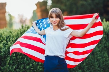 Amerikan bayrağıyla kameraya poz veren genç kadın.