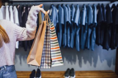 arka planda, raf giysileri ile kadının elinde hediye çantaları