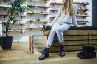 kot pantolon ve sıcak kazak, siyah çizmeler Ayakkabı mağazasında ayna önünde çalışan genç kadın