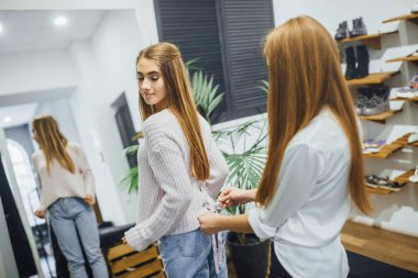 Satış Danışmanı şık dükkanda ayna önünde sıcak kazak seçmek yardım 