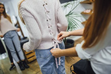 Satış Danışmanı şık dükkanda ayna önünde sıcak kazak seçmek için yardım