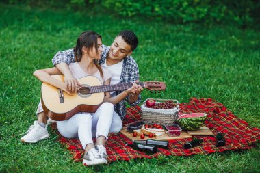 Romantik çift gitar çalmak parkta battaniye halı oturuyor 