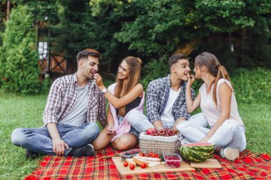 Mutlu arkadaşlar piknikte eğleniyor ve meyve yiyor, ön plana odaklanıyorlar.