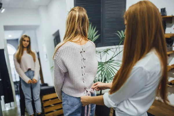 Satış Danışmanı şık dükkanda ayna önünde sıcak kazak seçmek yardım