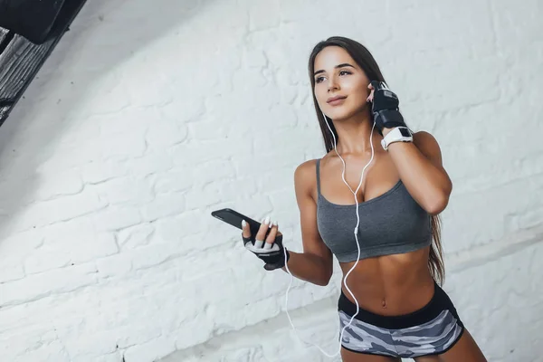 在健身房的智能手机上用耳机在运动服上听音乐的女人 — 图库照片