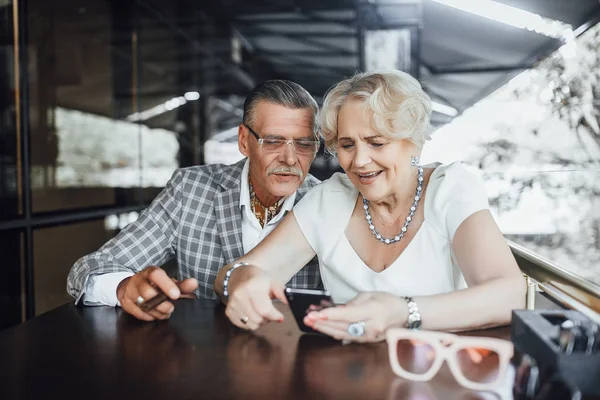 Beautiful couple searching something at phone sitting at summer terrace