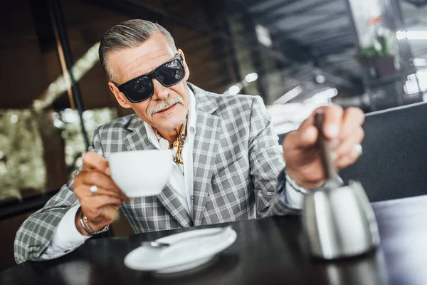 senior man drinking coffee on summer terrace in modern cafe