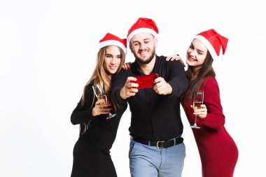 İki güzel kadın ve kırmızı noel şapkalı adam beyaz arka planda izole selfie yapma