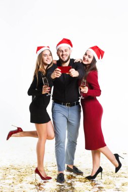 İki güzel kadın ve kırmızı noel şapkalı adam beyaz arka planda izole selfie yapma