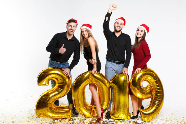 Portrait of group of friends celebrating New Year, standing with balloons with golden numbers in 2019 isolated on white background