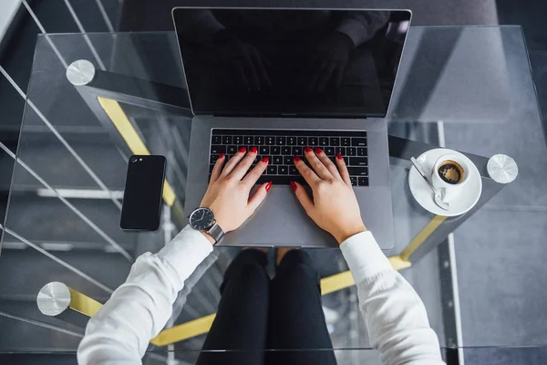 woman with black expensive watch, hands on glass table with laptop, smartphone and coffee