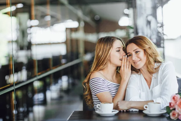 young beautiful daughter talking mom interesting secret at summer terrace cafe and laughing