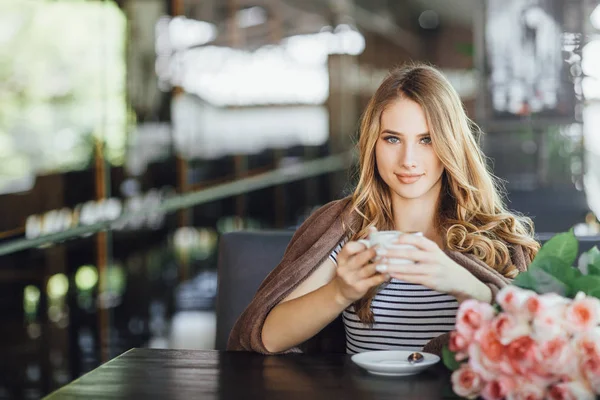 Young woman in casual clothes resting and drinking coffee on summer terrace