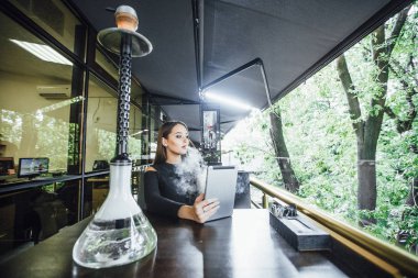 Modern restoranın yaz terasında dijital tablet ve sigara nargile kullanan genç kadın 