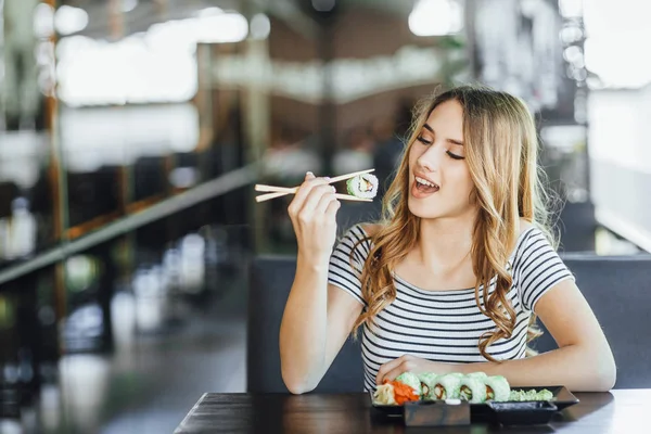 young beautiful woman eating sushi on summer terrace of Japanese restaurant