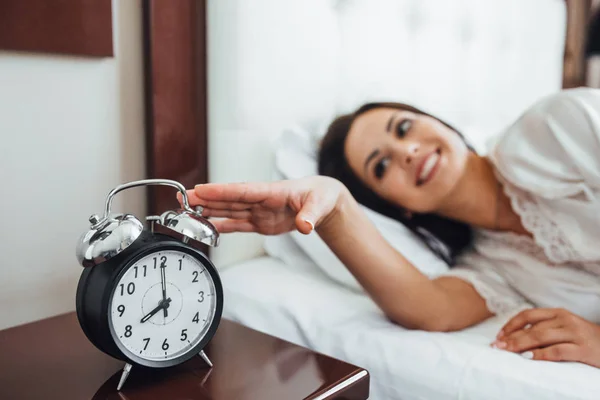 black alarm clock in morning, young brunette woman in background