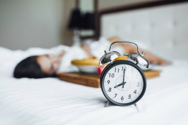 Siyah çalar saat, arka planda sabah yatakta yatan genç esmer kadın