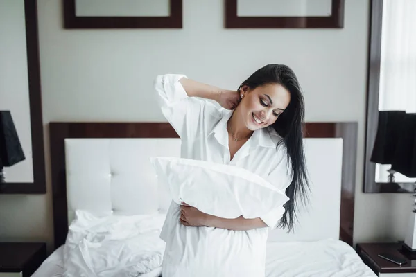 Portrait of beautiful brunette woman in bed with pillow in arms