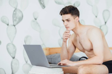 yatakta oturmuş ve sabah dizüstü bilgisayarda çalışan yakışıklı delikanlı