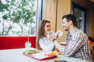 Seven genç çift birbirlerine hamburger ve patates, fast food Restoran pencerede yakınındaki gülümseyen besleme