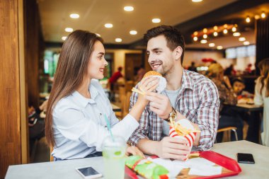 Seven genç çift birbirlerine hamburger ve patates, fast food Restoran pencerede yakınındaki gülümseyen besleme