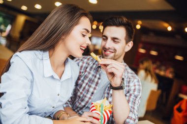 Hamburger ve patates hızlı restoranda yemek yerken zevk almak güzel gülümseyen Çift