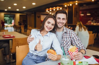 Hamburger ve patates hızlı restoranda yemek yerken zevk almak güzel gülümseyen Çift