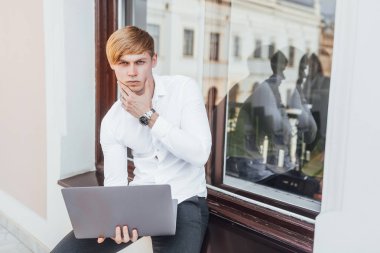 Pencerenin yanındaki sokakta dizüstü bilgisayarları olan genç ve şık bir iş adamı.