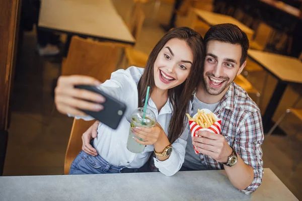 年轻夫妇在手机上自拍与莫吉托和汉堡包 微笑着在快餐咖啡馆 选择性的焦点 — 图库照片