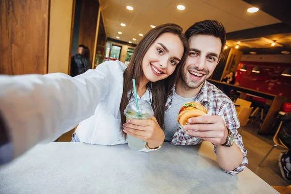 年轻夫妇在手机上自拍与莫吉托和汉堡包 微笑着在快餐咖啡馆 选择性的焦点 — 图库照片