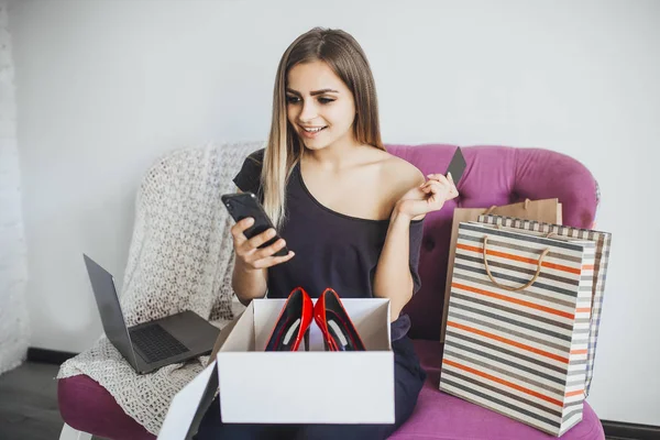 beautiful woman with credit card and mobile phone in hands unpacking new red shoes