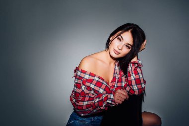 gri arka plan üzerinde oturan rahat tarzı itibariyle giymiş esmer kadın