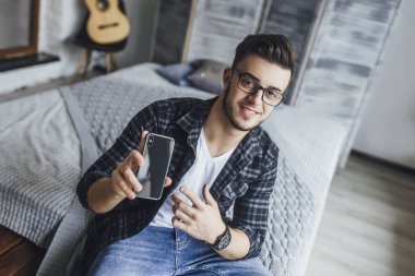 Yeni cep telefonu çatı odasında gösterilen gözlüklü genç yakışıklı blogger