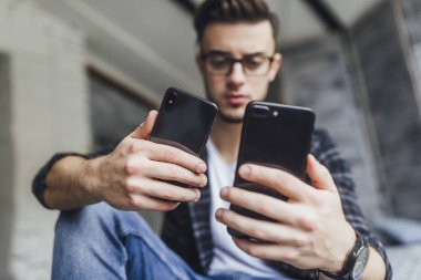 Çatı odasında iki cep telefonu karşılaştırma gözlüklü genç yakışıklı blogger