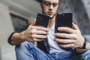 Çatı odasında iki cep telefonu karşılaştırma gözlüklü genç yakışıklı blogger