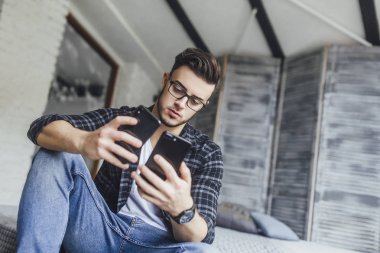 Çatı odasında iki cep telefonu karşılaştırma gözlüklü genç yakışıklı blogger