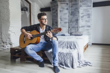 Gülümseyen ve yatakta gitar ile poz gözlüklü genç yakışıklı adam 