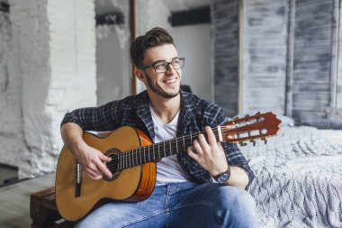 Gülümseyen ve gitar yatakta Studio ile poz gözlüklü genç yakışıklı adam
