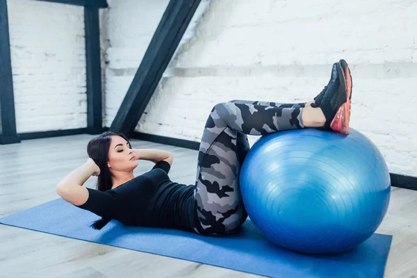 Young woman in fitness wear exercising with blue fitness ball