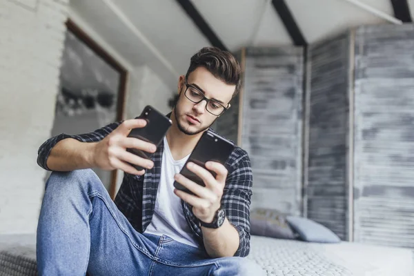 Çatı odasında iki cep telefonu karşılaştırma gözlüklü genç yakışıklı blogger