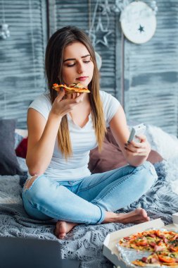 kadın evde laptop ve yeme pizza yakın yatakta oturan