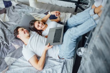 Evde yatıp dizüstü bilgisayar kullanan genç bir çift.
