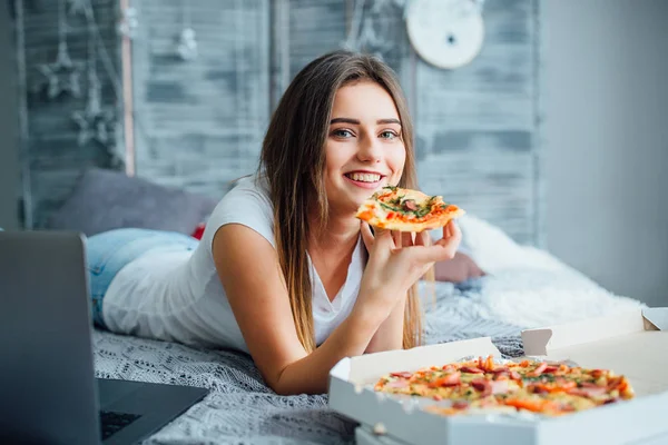 ラップトップの近くにベッドの上に座って 自宅でピザを食べている女性 — ストック写真