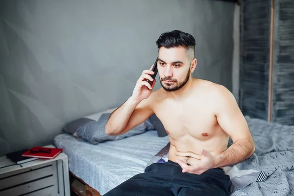 Junger Mann Sitzt Auf Bett Und Telefoniert Mit Smartphone — Stockfoto